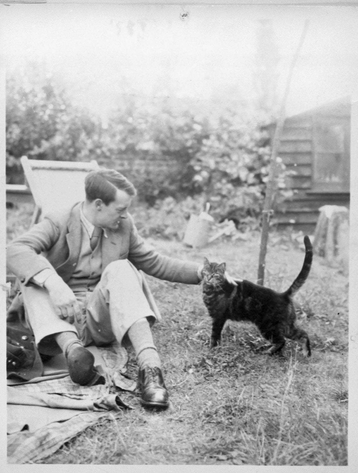Black-and-white photograph of Eric Ravilious sitting in a garden with a cat